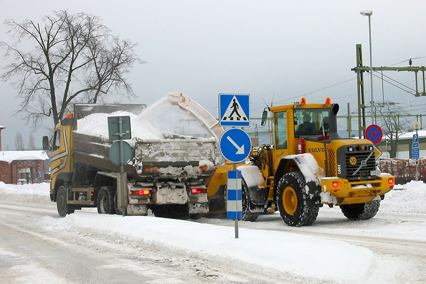 vintergata med snö, lastbil och en grävmaskin som lastar snö